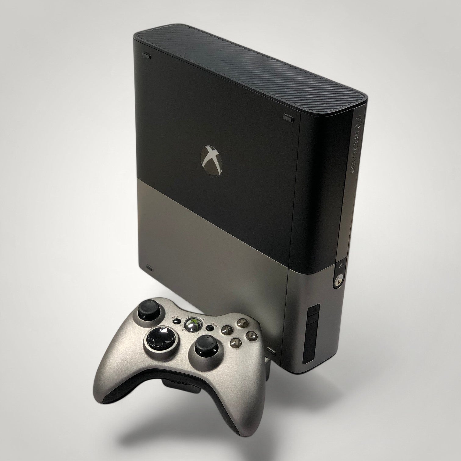 StudioFR customized black and grey Xbox 360E console with matching controller. Features a window mod with RGB lighting.