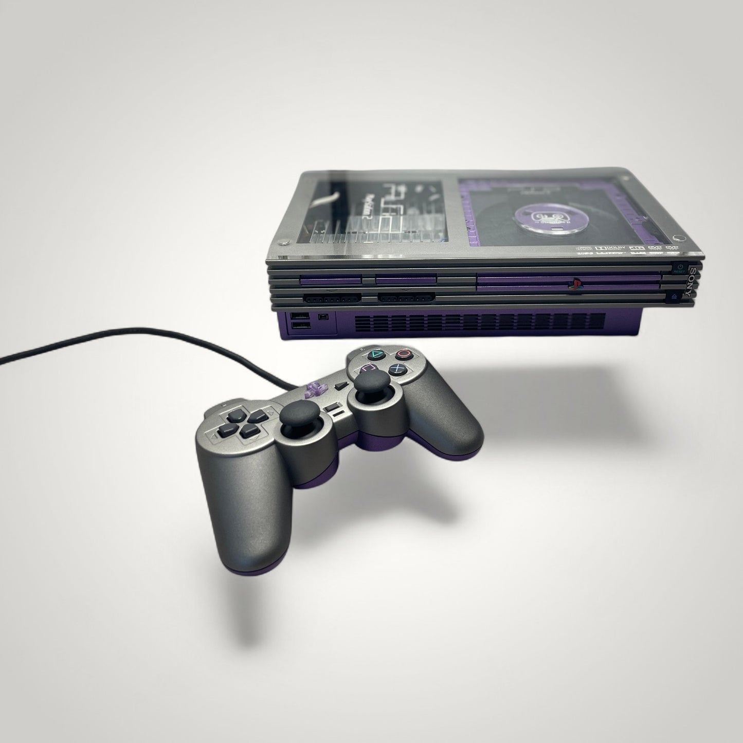 StudioFR custom purple and grey PlayStation 2 Fat console with matching controller. Features RGB lighting and custom acrylic top.