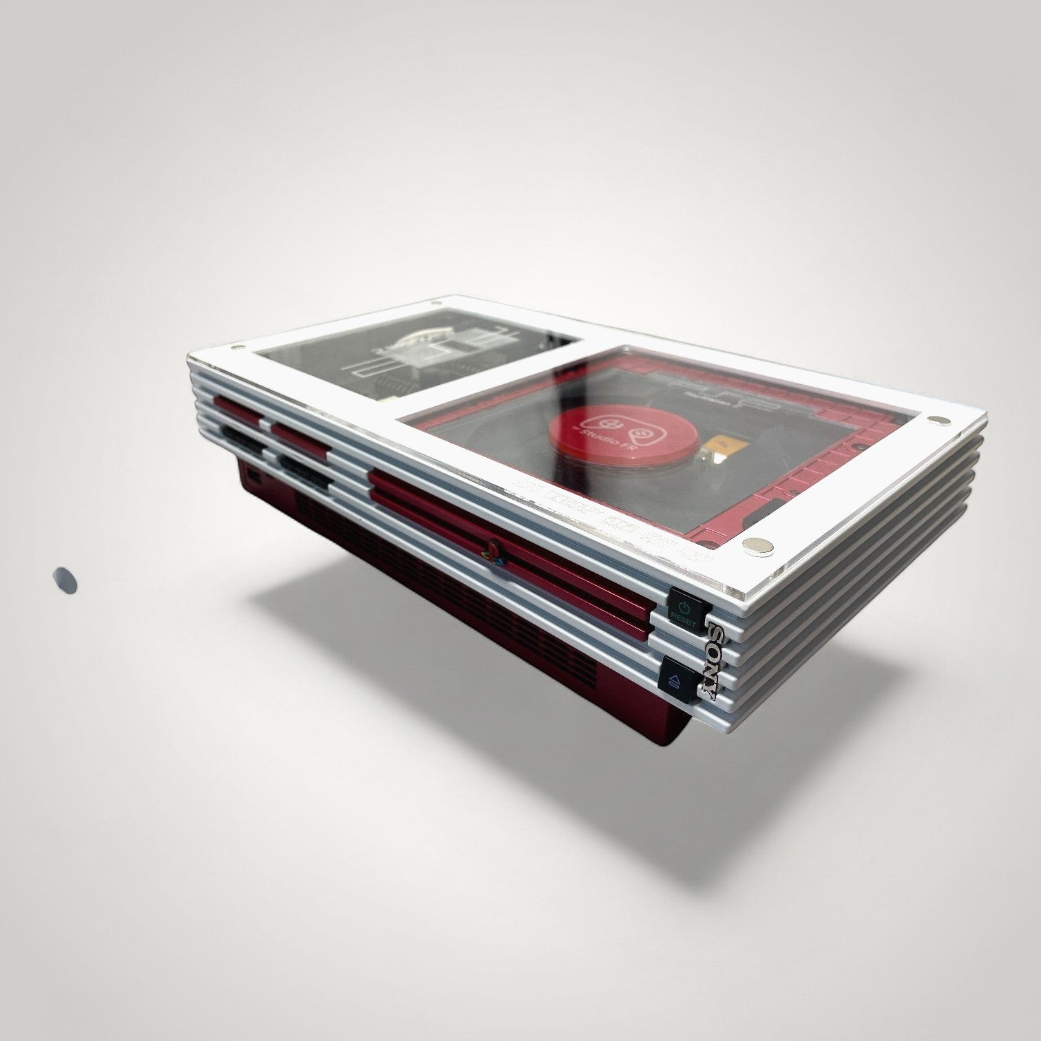 StudioFR customized red and white PlayStation 2 Fat console with clear top showing internal components and RGB lighting.