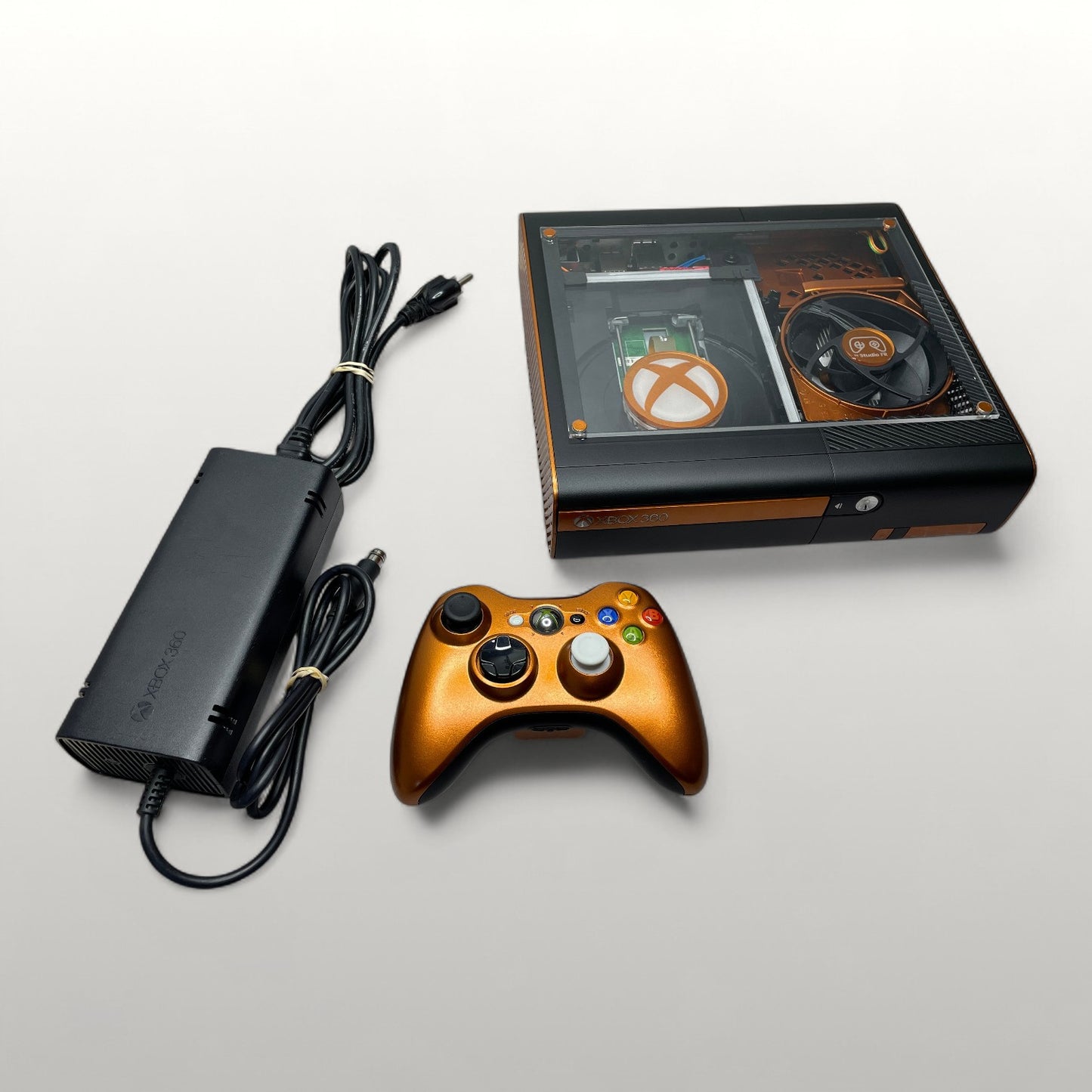 StudioFR custom black and copper Xbox 360E console with clear window mod and matching controller.
