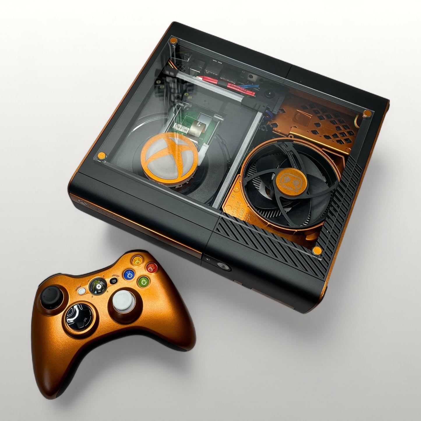 StudioFR customized Xbox 360E console in black and copper with a clear top window showing internal components and RGB lighting. Includes matching copper controller.