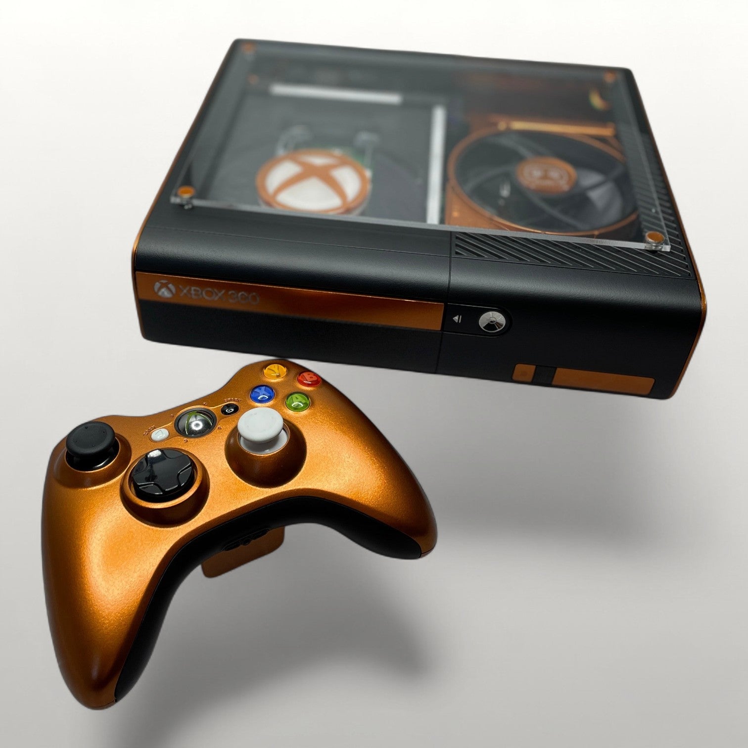 StudioFR custom black and copper Xbox 360E console with matching controller. Features a clear top window with RGB lighting.