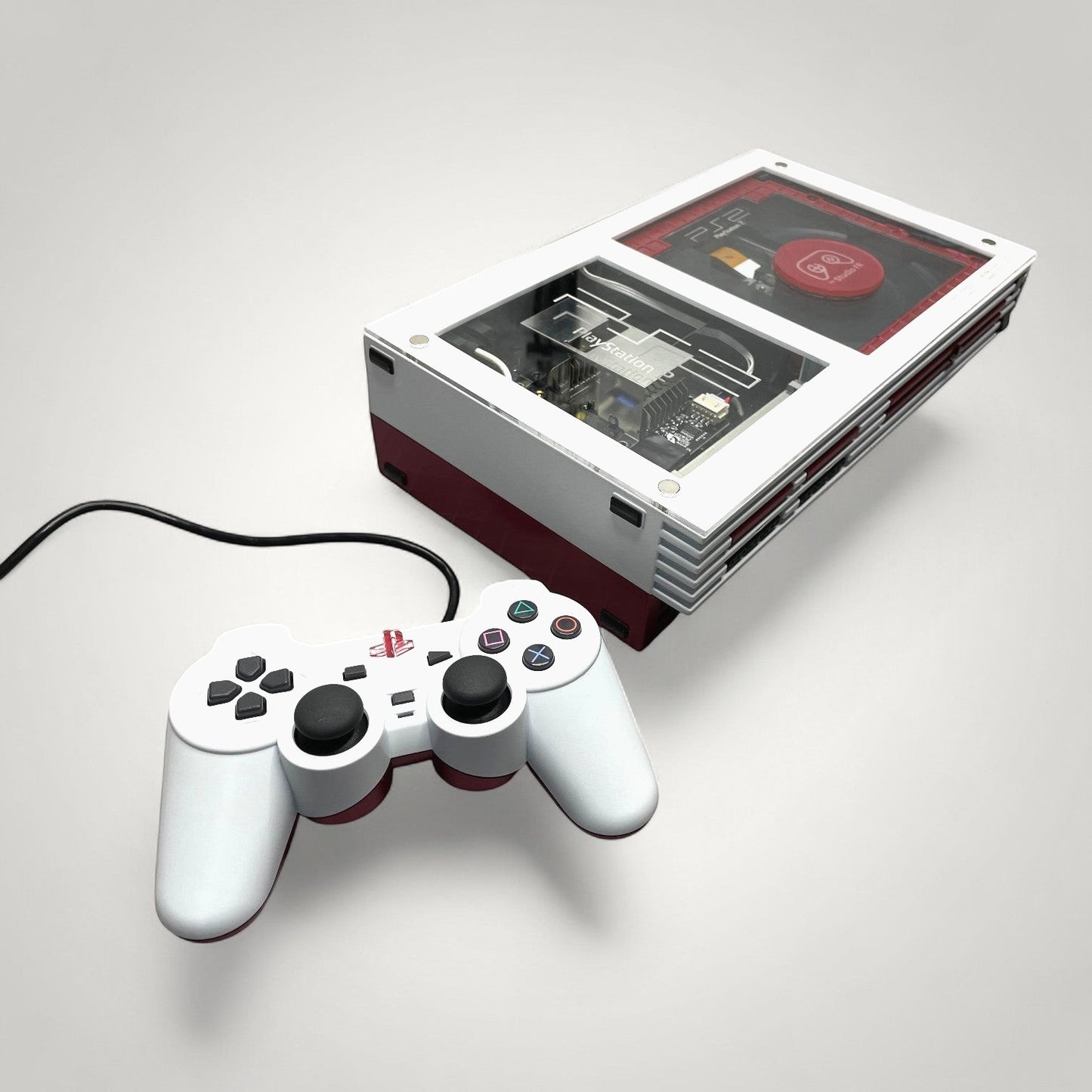 StudioFR custom red and white PlayStation 2 Fat console with clear top and matching controller.